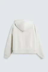 Sudadera con capucha color crudo, corte boxy, manga larga y bolsillo tipo canguro.