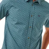 Camisa de manga corta color verde con estampado de micro triángulos blancos. Tiene cuello clásico, cierre con botones y bolsillo en el pecho.
