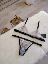 Conjunto de lencería color tostado con detalles en negro, compuesto por un corpiño triangular de encaje con breteles finos y una tanga de encaje con tiras laterales ajustables.