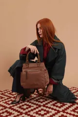 Mochila bandolera color marrón con herrajes color peltre. Tiene un compartimento principal amplio con cierre, un bolsillo frontal con cierre y dos bolsillos laterales abiertos. Incluye correa ajustable para usar al hombro o cruzada.