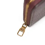 Billetera tipo fichero de material sintético (PU) color bordó, con textura granulada. Presenta cierre perimetral metálico dorado y un logo XL metálico aplicado al frente.