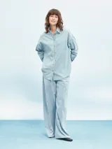 Camisa celeste de denim con botones marrones, corte holgado y mangas largas.