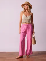 Pantalón ancho de lino color rosa vibrante, con cintura elastizada y cordón ajustable. Presenta un ruedo con tajo y flecos deshilachados.