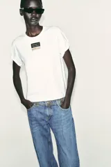 Camiseta blanca de manga corta y cuello redondo. Estampado frontal con etiqueta negra y dorada.