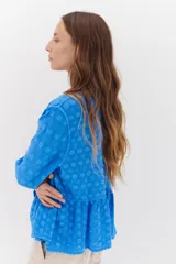 Camisa celeste de algodón con textura arrugada y bordados a tono, escote amplio, mangas largas y botones frontales.