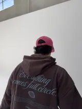 Gorro tipo gorra color fucsia con visera, y estampado frontal en azul con la palabra "attitude" y otros textos.