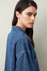 Sobrecamisa oversize de jean azul con cuello camisero, cierre frontal con botones, mangas largas y bolsillos de parche en el pecho.