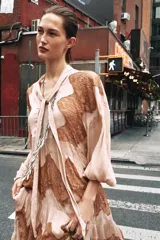 Vestido midi color beige con detalles de encaje marrón, cuello alto con lazo, escote pico, manga larga y botones frontales.