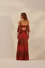 Vestido largo color ladrillo con escote halter, espalda descubierta y falda con tres niveles de flecos.