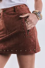 Mini pollera marrón de gamuza con tachas doradas, cierre lateral con cremallera y corte ajustado.