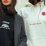 Canguro oversize color crudo con capucha y cordones ajustables. Estampado en la espalda con tres flores rojas, la frase "Lookmom Street" y un texto motivacional.