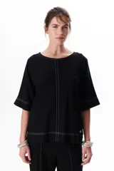 Blusa de lino color beige claro, con mangas 3/4 y cuello redondo. Presenta pespuntes a contratono en el centro, puños y ruedo.