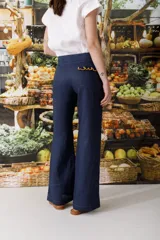 Pantalón de jean azul oscuro, de corte acampanado, con bolsillos delanteros con detalle de volados.