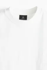 Remera blanca de algodón pesado, corte holgado, cuello redondo ribeteado, hombros caídos y bajo recto.