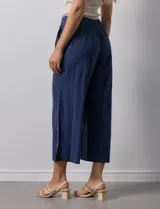Pantalón blanco de algodón con pretina elastizada, bolsillos inclinados y ruedo lateral con tajo y botones.