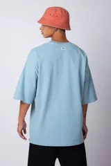 Remera verde militar de corte oversize, confeccionada en algodón 100% con cuello redondo y manga corta. Presenta un pequeño logo estampado en la parte superior de la espalda.