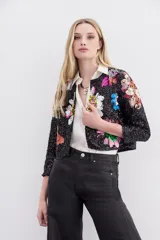 Saco corto negro de poliéster cubierto de paillettes, con cuello redondo y cierre frontal con ganchos invisibles. Presenta bordados florales multicolores hechos a mano en frente, espalda y mangas.