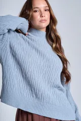 Sweater color crema de punto trenzado, con cuello alto y mangas largas.