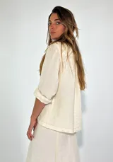 Chaqueta color gris con textura, de corte recto, cuello camisero, cierre frontal con botones, mangas 3/4 con puños arremangados, dos bolsillos de parche en el pecho y ruedo recto.