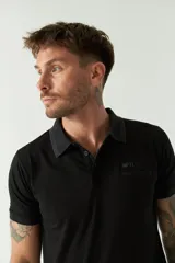 Remera polo negra de manga corta con cuello clásico, cierre de botones, bolsillo en el pecho y logo estampado.