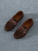 Zapato estilo mocasín acordonado, confeccionado en pelo color marrón con interior forrado en cuero vacuno. Lleva apliques metálicos en níquel.