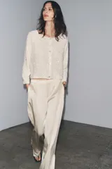 Chaqueta color crema de tejido de punto con lentejuelas, cuello barco, manga larga y cierre frontal con botones.