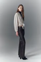 Pantalón jeanero de cuero ovino color marrón oscuro, de calce flare con efecto gastado y tachas aplicadas.