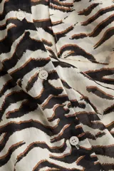Camisa de manga larga con estampado de cebra en tonos blanco y negro. Tiene cuello clásico, cierre frontal con botones y un bolsillo de parche en el pecho.