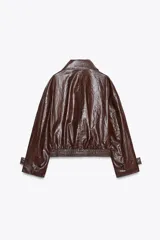 Chaqueta de Zara Woman Collection en tejido con acabado brillante efecto cuero. Presenta cuello solapa, manga larga con trabillas ajustables, bolsillos delanteros y cierre frontal con botones ocultos bajo solapa.