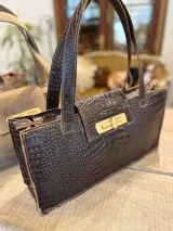 Bolso tote marrón con textura símil cocodrilo, cierre dorado y doble asa de mano.