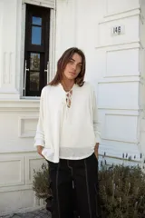 Blusa blanca de lino con mangas largas con elástico en los puños, escote en V con doble lazo y bajo asimétrico.