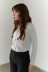 Remera blanca de mangas largas con escote en V y costuras decorativas en negro.