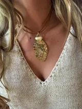 Collar con colgante dorado en forma de hoja con perforaciones y cordón marrón.