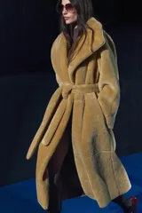 Abrigo largo color camel con efecto piel de oveja, cuello solapa, manga larga, bolsillos delanteros y cinturón ajustable con lazadas. Forro interior.