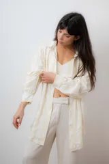 Conjunto de camisa y top corto a rayas verticales amarillas y blancas. El top es corto con tiras finas y elástico en la base. La camisa es de manga larga y corte relajado.