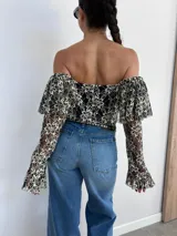 Top corto negro con diseño de encaje floral en blanco, escote bardot y mangas largas acampanadas.