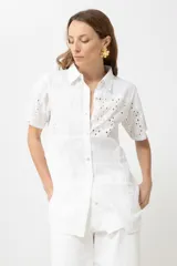 Camisa verde con cuello clásico, manga corta y cierre frontal con botones. Presenta diseño patchwork con detalles de broderie y calados.