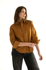 Camisa marrón de corte clásico, con cuello, mangas largas con puños abotonados, cierre frontal con botones al tono, bolsillo de parche en el pecho y ruedo redondeado.