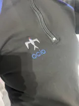 Remera térmica negra de manga larga con cierre frontal parcial, vivos en contraste color azul y logo bordado.