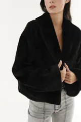 Abrigo de peludito negro, con corte corto y mangas largas, ideal para abrigarse en invierno.
