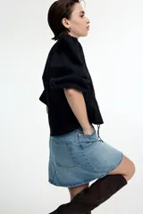 Blusa negra de algodón con textura de lunares, escote redondo con lazo, mangas tres cuartos abullonadas, botones frontales y cintura ajustable con cordón.