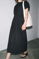 Vestido midi color marrón confeccionado en hilatura con mezcla de algodón y lino. Tiene cuello redondo, manga corta caída y detalle de pliegues en la cintura. Cierre en la espalda con abertura y botón.
