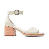 Sandalias de cuero sintético color hueso, con punta descubierta, tira ancha sobre los dedos, pulsera al tobillo con hebilla metálica y taco geométrico color madera clara.