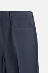 Pantalón de vestir azul marino, de corte recto, con pinzas frontales, bolsillos laterales y traseros de ojal. Se cierra con cremallera y doble botón.