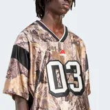 Camiseta de fútbol Adidas Originals con estampado de camuflaje en tonos marrones y negros. Tiene cuello en V con ribete blanco, mangas cortas con rayas negras en los hombros y el número 03 estampado en el frente.