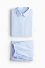 Conjunto de pijama de dos piezas en popelina de algodón a rayas celestes y blancas. La camisa es de manga larga con cuello clásico, hombros caídos y botones en delantero y puños. El pantalón tiene elástico en la cintura, cordón para ajustar y piernas amplias con vuelo en los bajos.