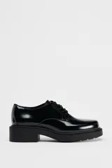 Zapato tipo mocasín negro acharolado con punta redonda y cierre de cordones. Suela de 4 cm de altura.