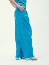 Pantalón de vestir color crema, de corte ancho y tiro alto, con pinzas delanteras y cinturón fino de cuero marrón.