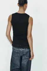 Camiseta ajustada (slim fit) de cuello redondo y manga sisa, color beige claro, con frunces laterales y bajo asimétrico con terminación de encaje a tono.