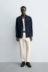 Pantalón chino negro de corte relajado (relaxed fit) con tiro medio, confeccionado en algodón con elasticidad. Presenta bolsillos delanteros y bolsillos traseros de vivo, con cierre frontal de cremallera y botón.